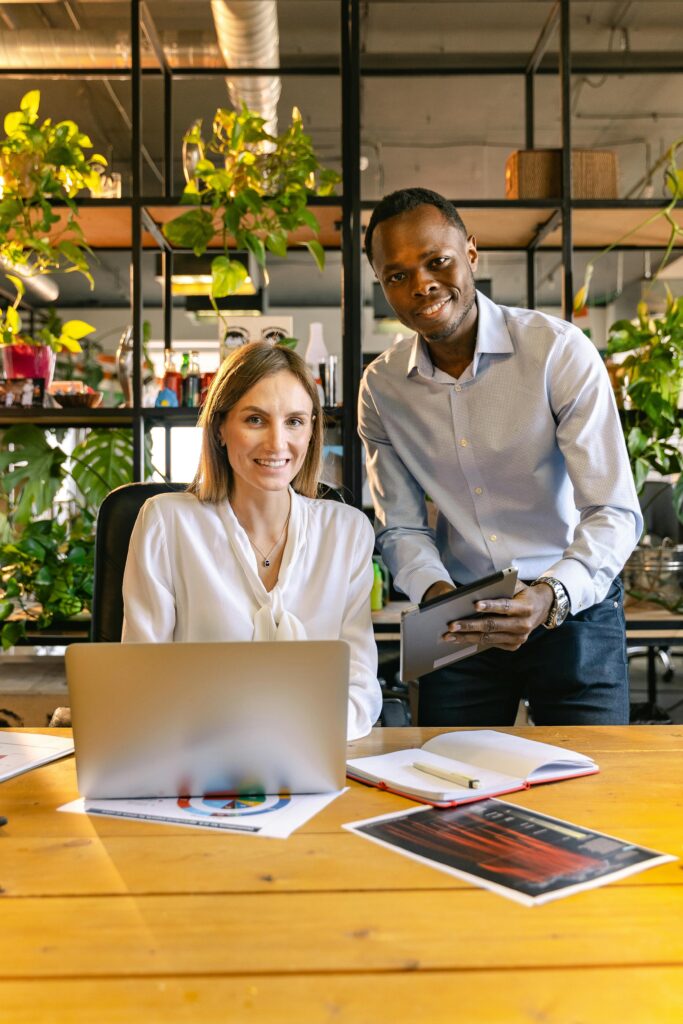 Two professionals at a desk collaborating in a plant-filled modern office environment.
